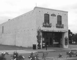 Lompoc Valley Chamber of Commerce building, two-story stucco, arched windows, sign above entrance, rose bushes in foreground.