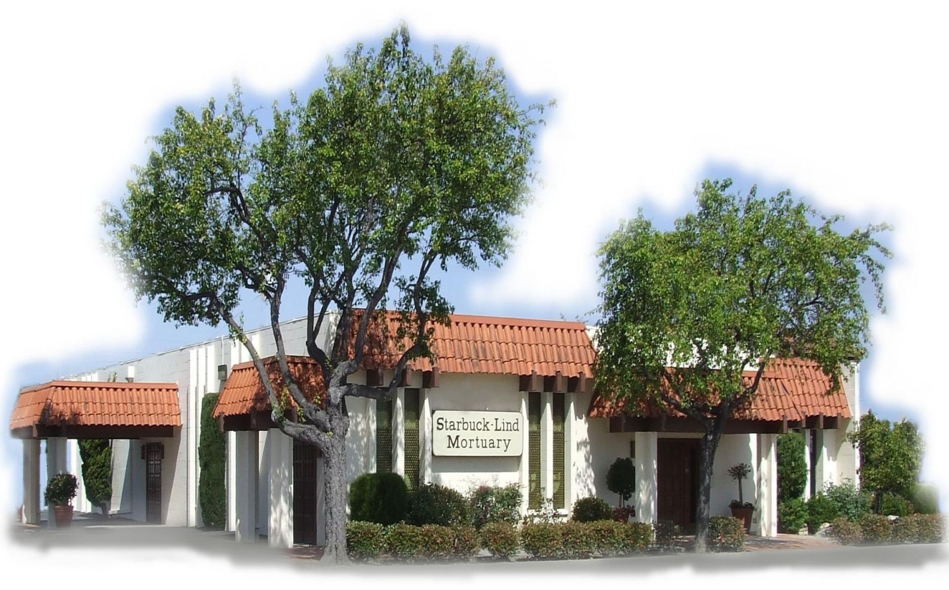 A white building with a red-tiled roof, greenery, and the words 