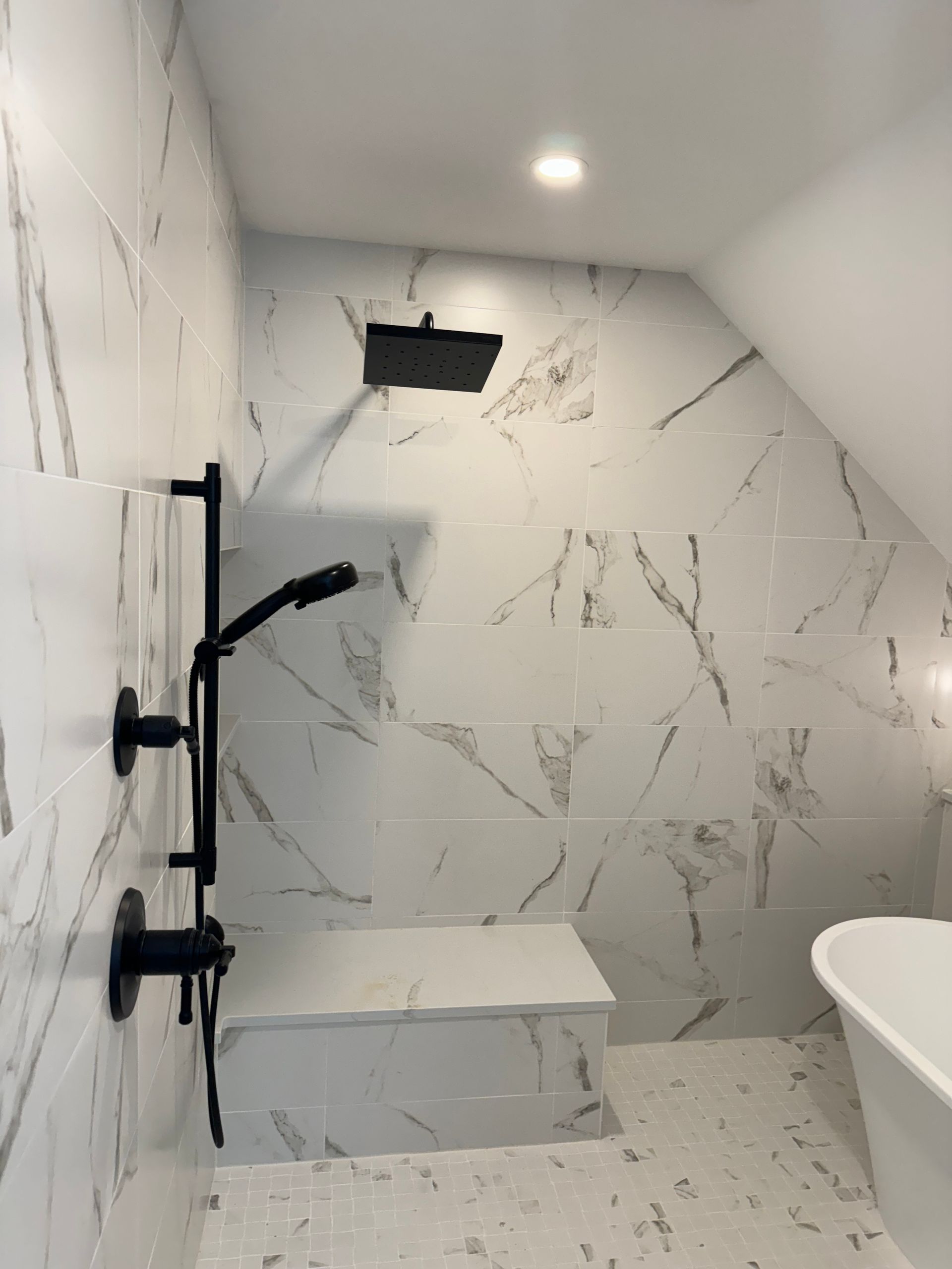 Modern tiled walk-in shower with black fixtures, bench, and wall niche under a ceiling light