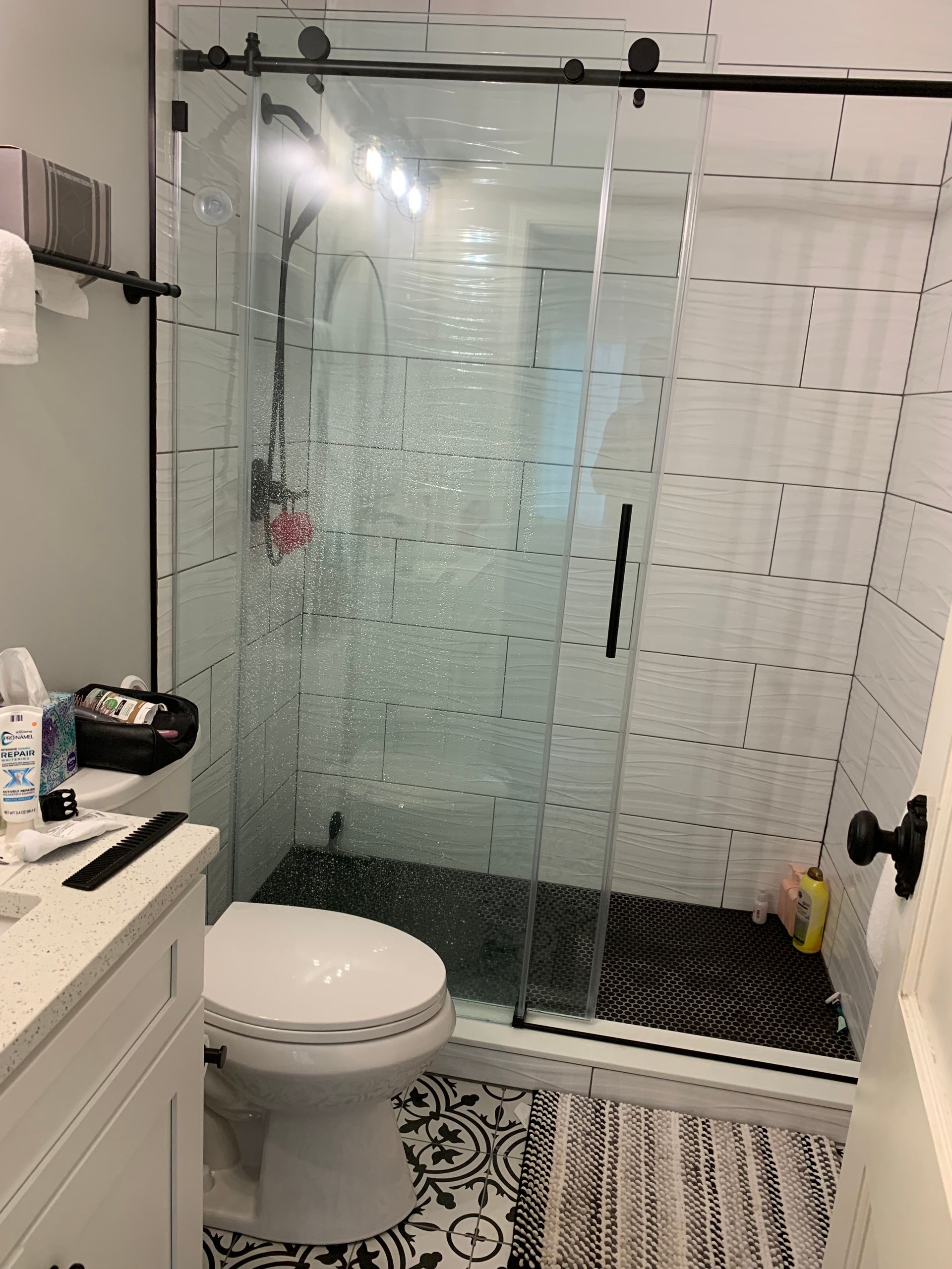 Small bathroom with glass shower enclosure, toilet, vanity, and patterned floor tiles.