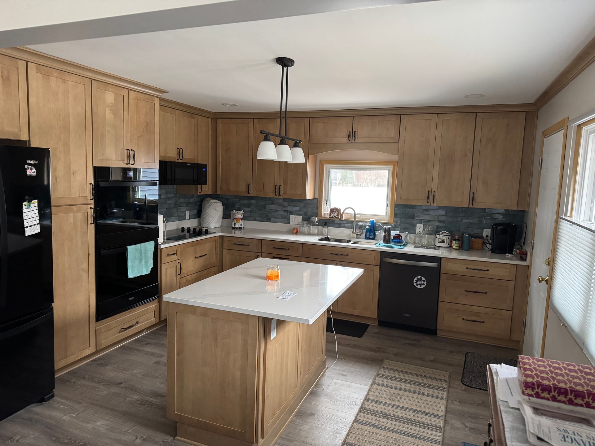 Bright kitchen with wood cabinets, black appliances, a white island, and a window over the sink.