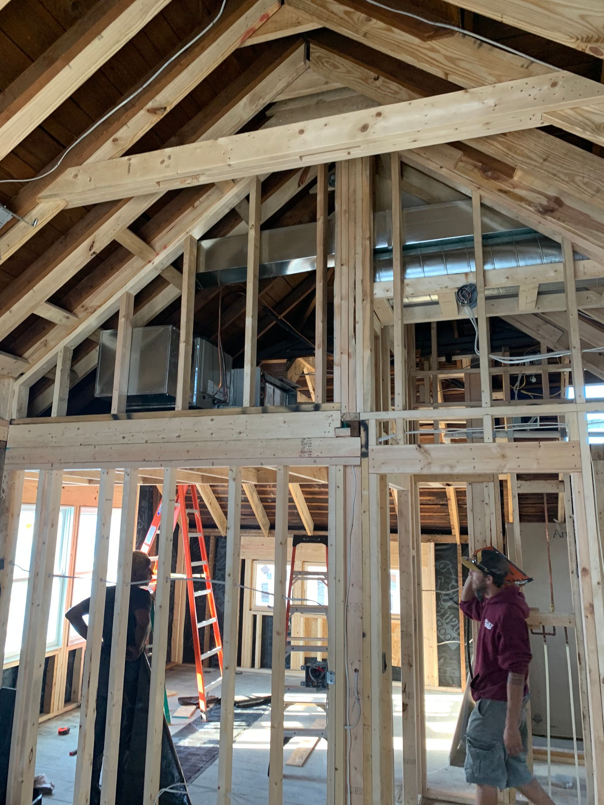Interior of a house under construction with exposed wooden framing and two workers inside.