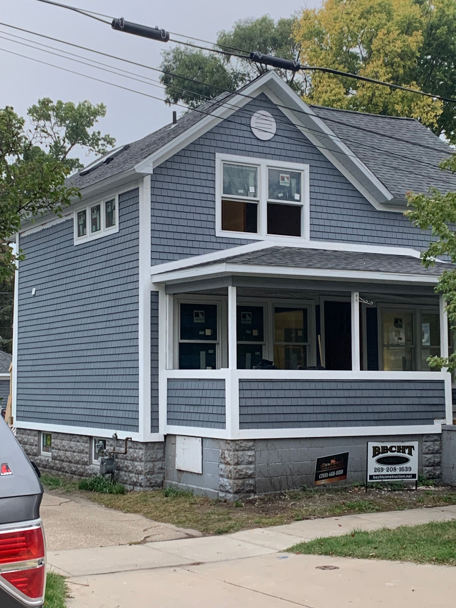 Gray two-story house with white trim and stone foundation on a residential street