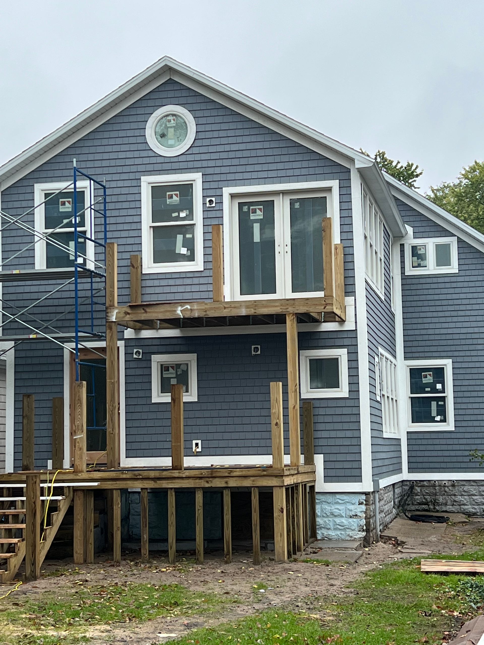 Blue-gray house exterior with white trim, front porch, and wooden deck framing under construction