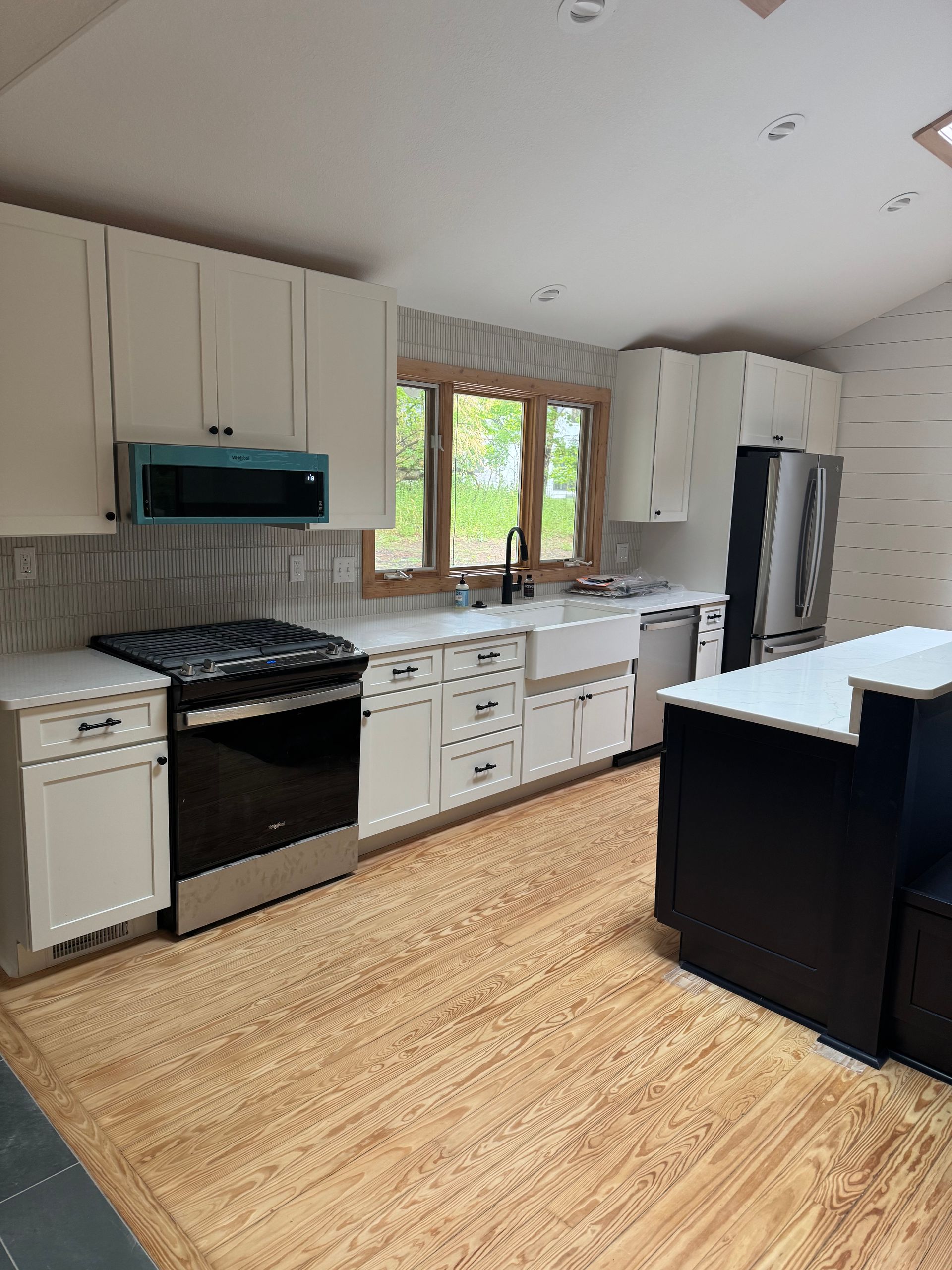 Bright white kitchen with black appliances, island, and large window over the sink