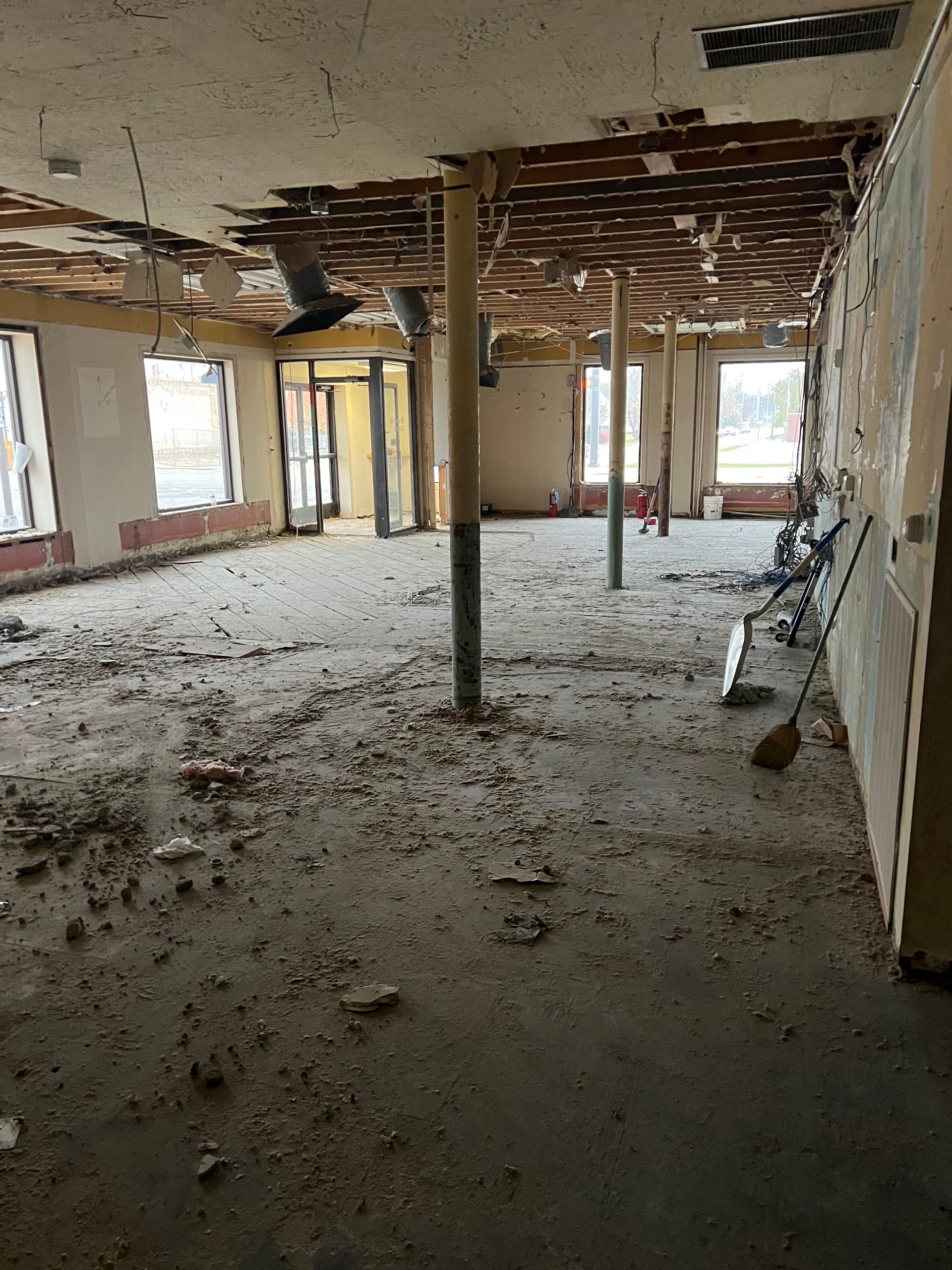Debris-filled room under renovation with exposed ceiling, support poles, and unfinished walls