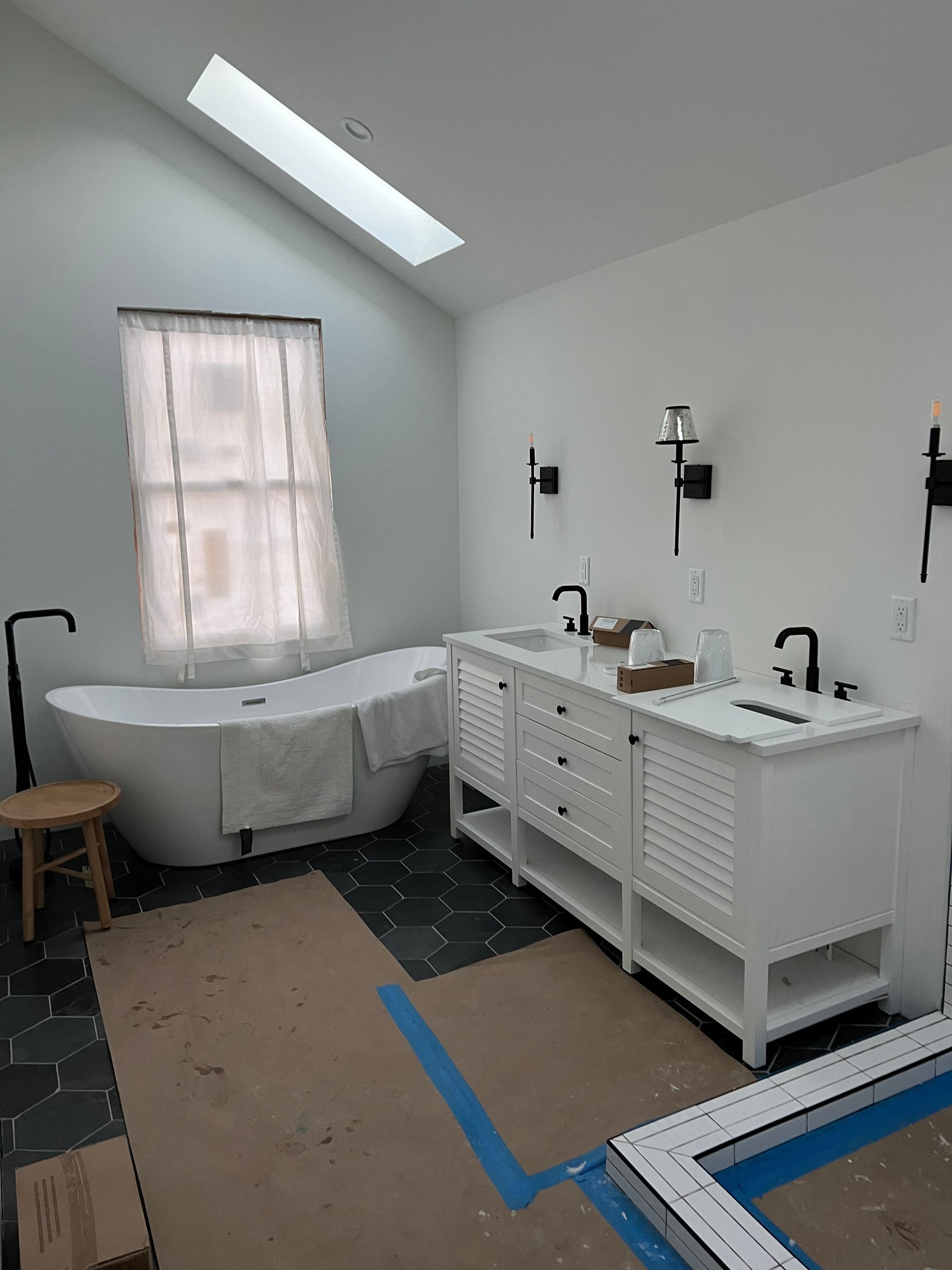 Modern white bathroom with freestanding tub, vanity sinks, large mirror, and skylight.