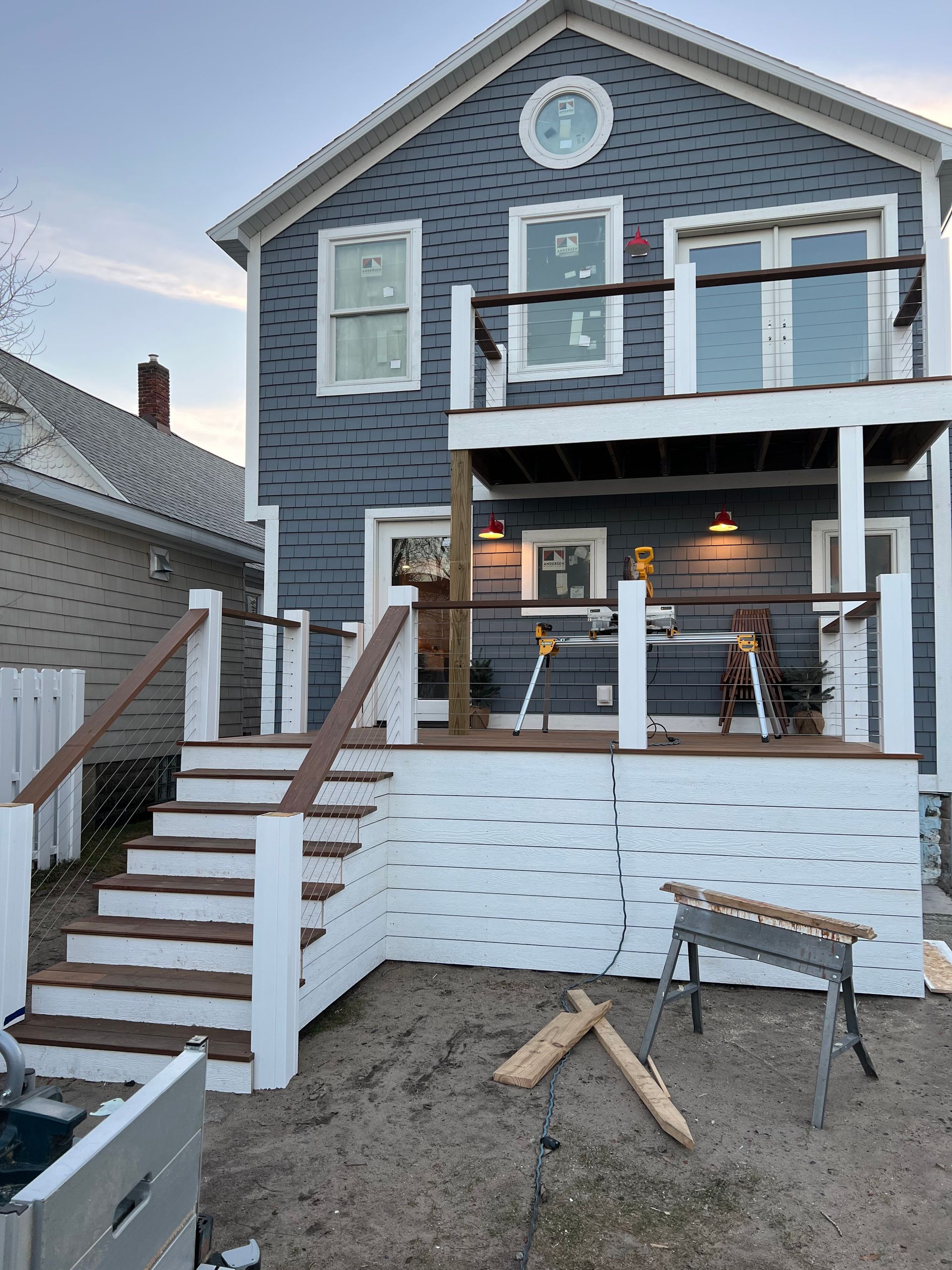 Two-story gray house with white trim and a front porch, stairs, and a snowy yard under construction