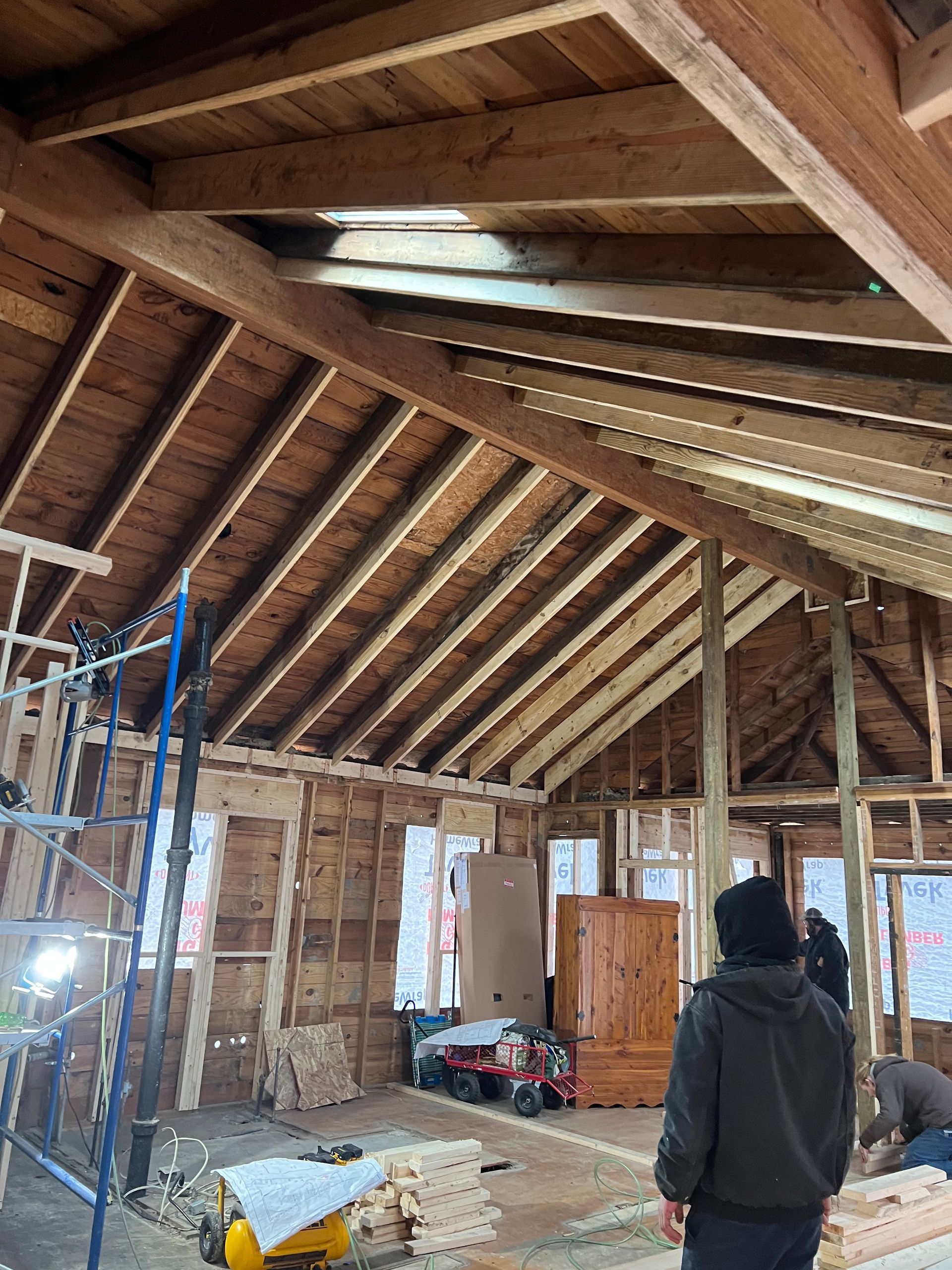 Attic interior under construction with exposed wood rafters, scaffolding, tools, and a person in a dark jacket