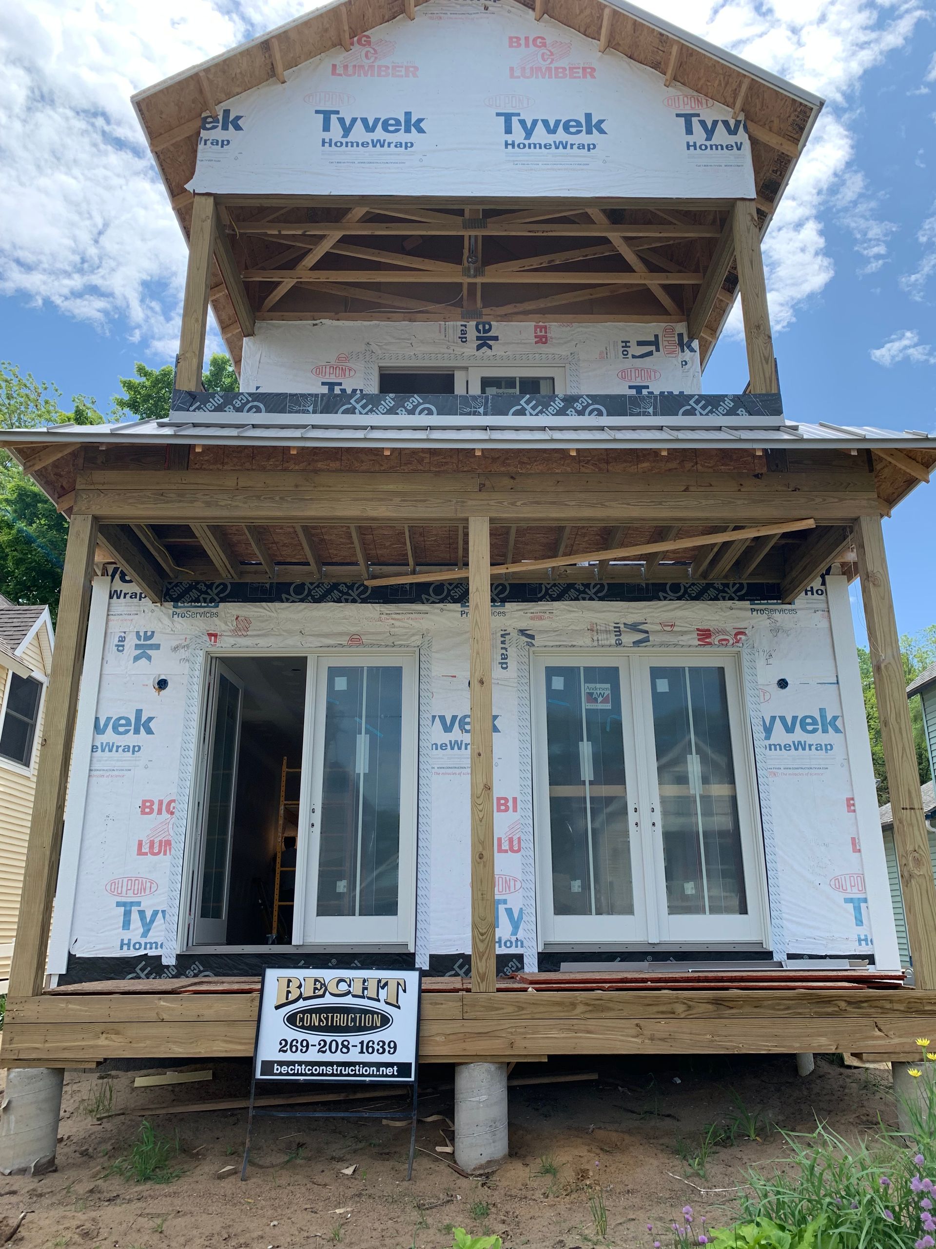 Partially built two-story house under construction with exposed framing and Tyvek wrap