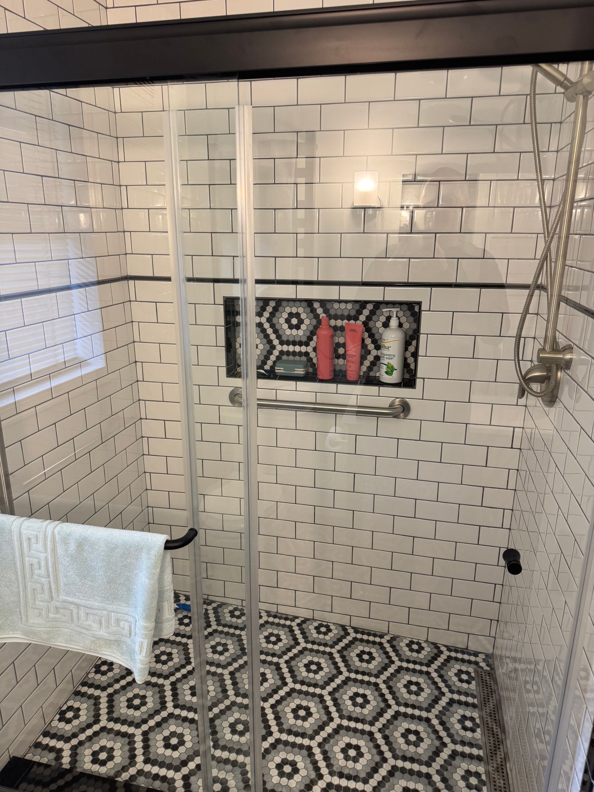 Modern bathroom with white tile, black patterned floor, a shower curtain, and a small wall mirror with a red towel.