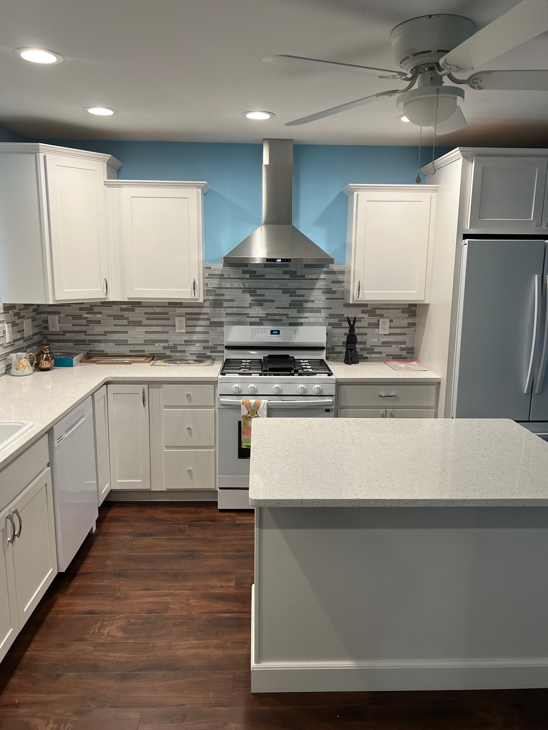 Bright modern kitchen with white cabinets, gray island, stainless appliances, and wood floors.