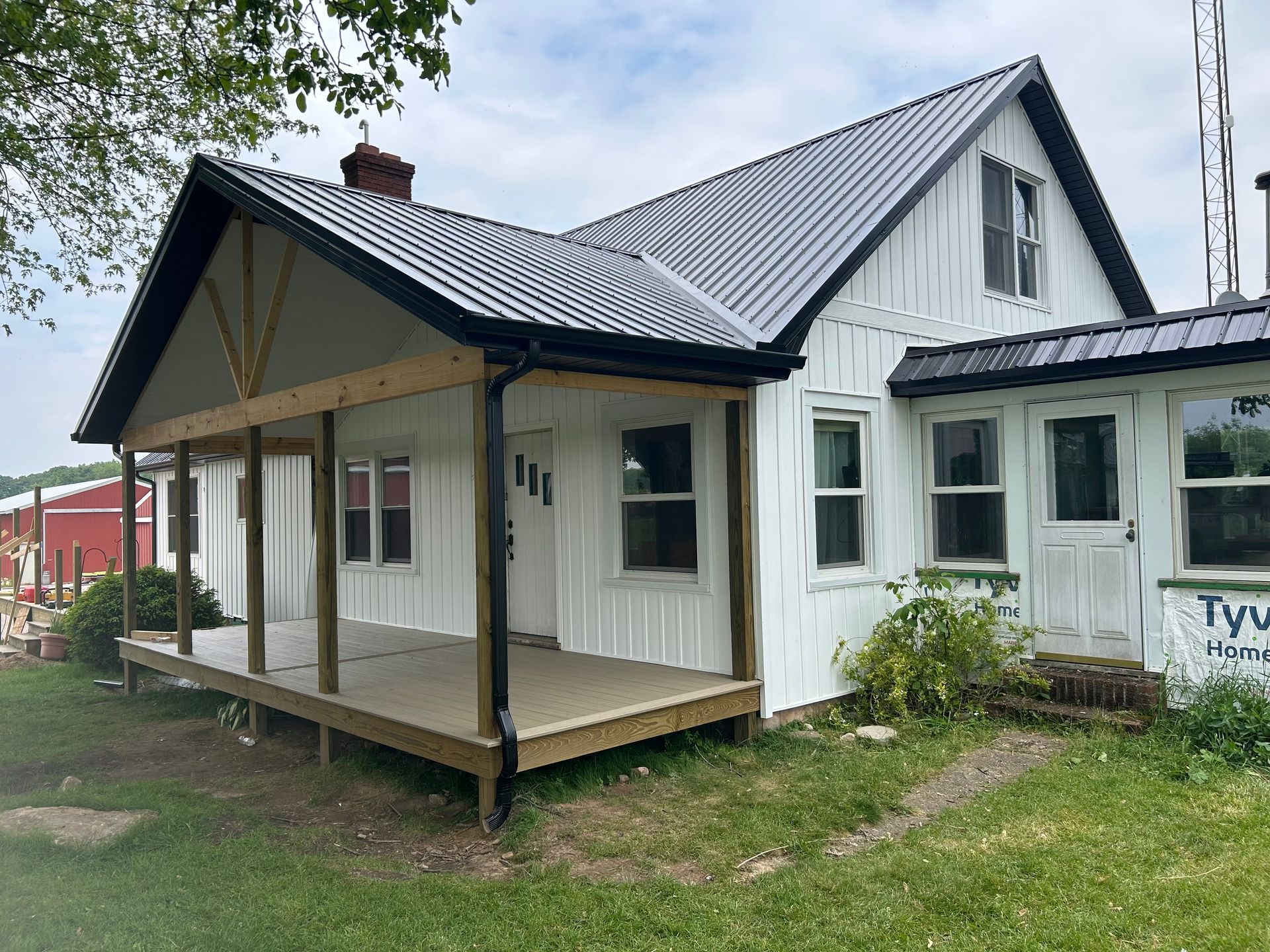 White farmhouse with a gray metal roof and front porch on a grassy lot under cloudy skies