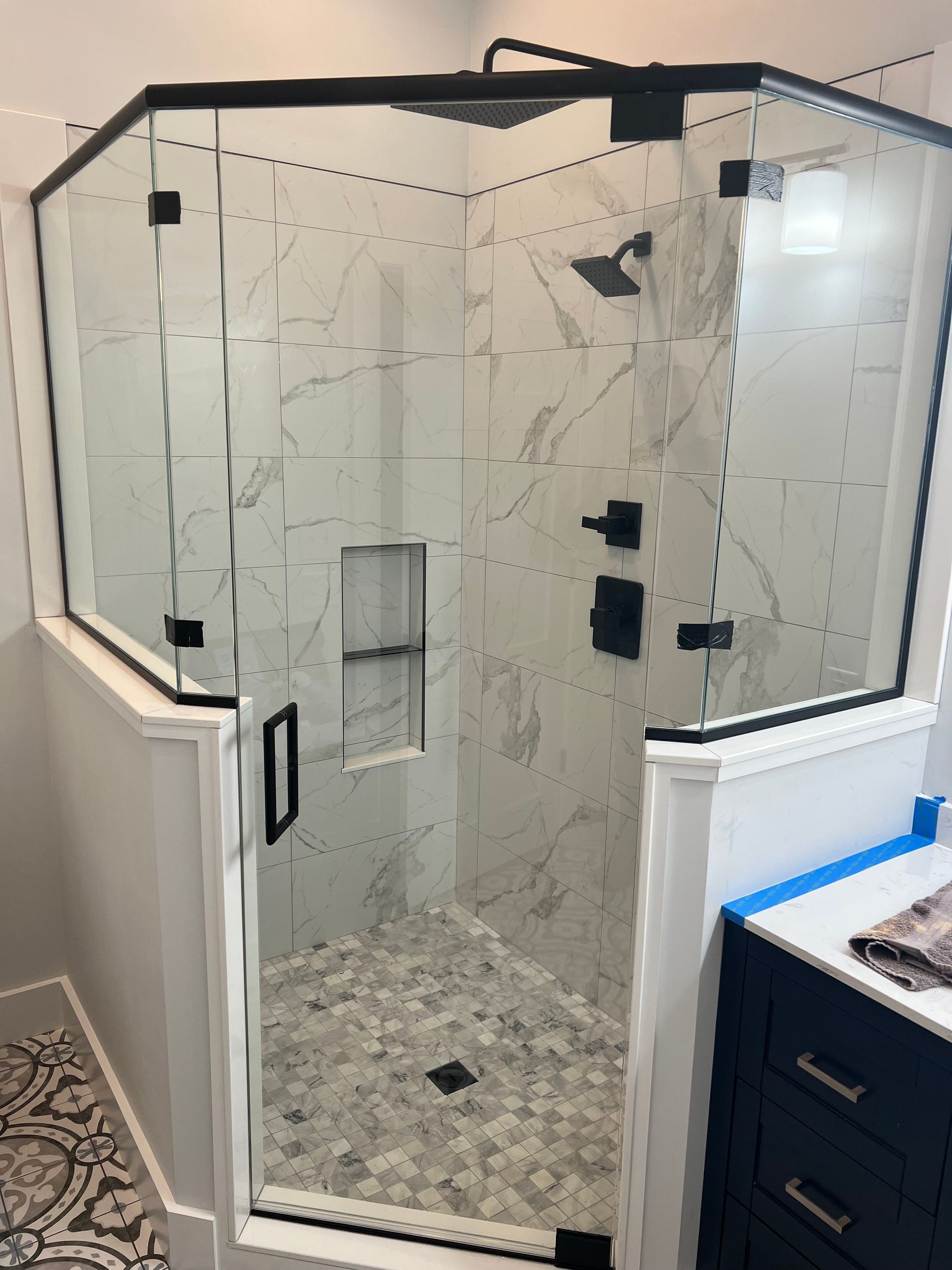 Glass shower enclosure with white tile walls and hexagon tile floor in a bathroom