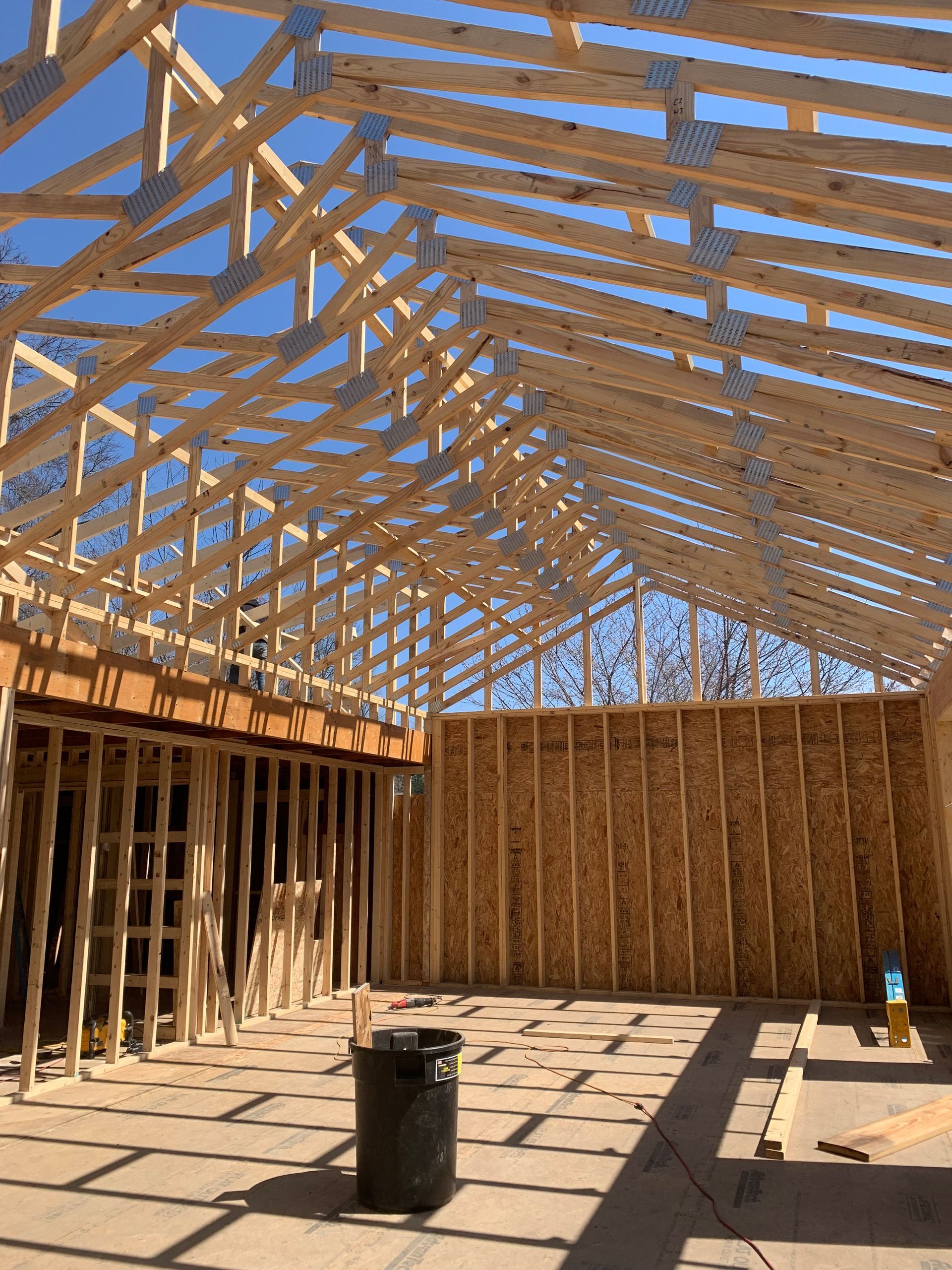 Wood-framed house under construction with exposed trusses and unfinished walls in sunlight