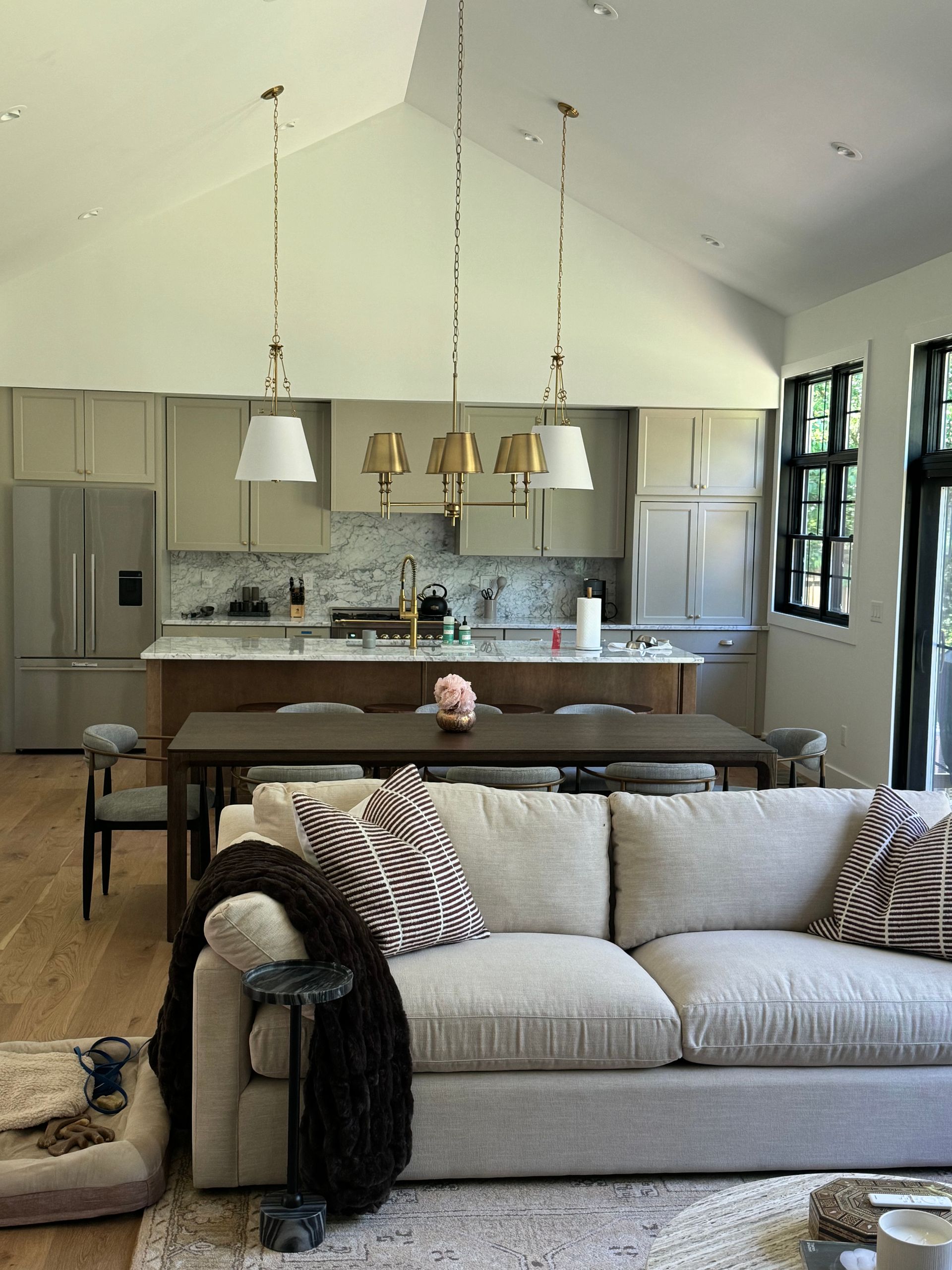 Bright open kitchen and living room with gray sofa, island, pendant lights, and large windows