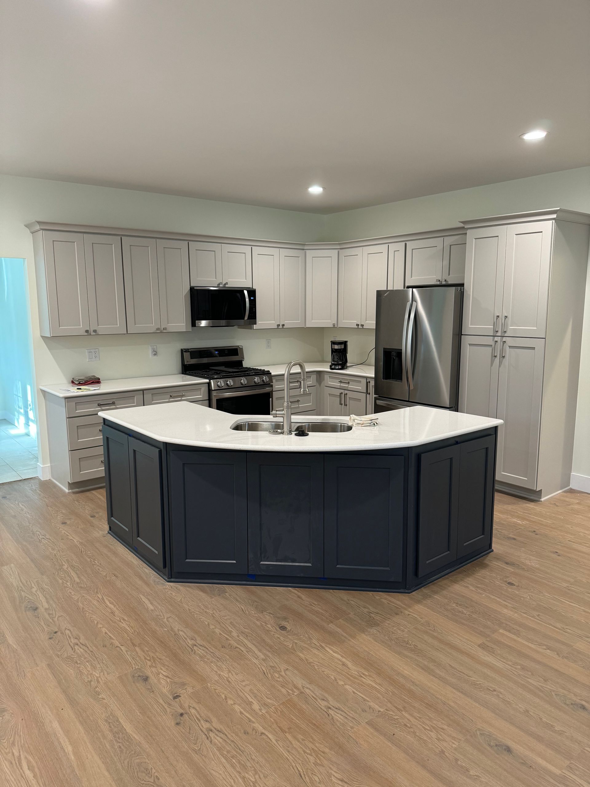 Modern kitchen with white cabinets, stainless steel appliances, and a navy island on wood flooring