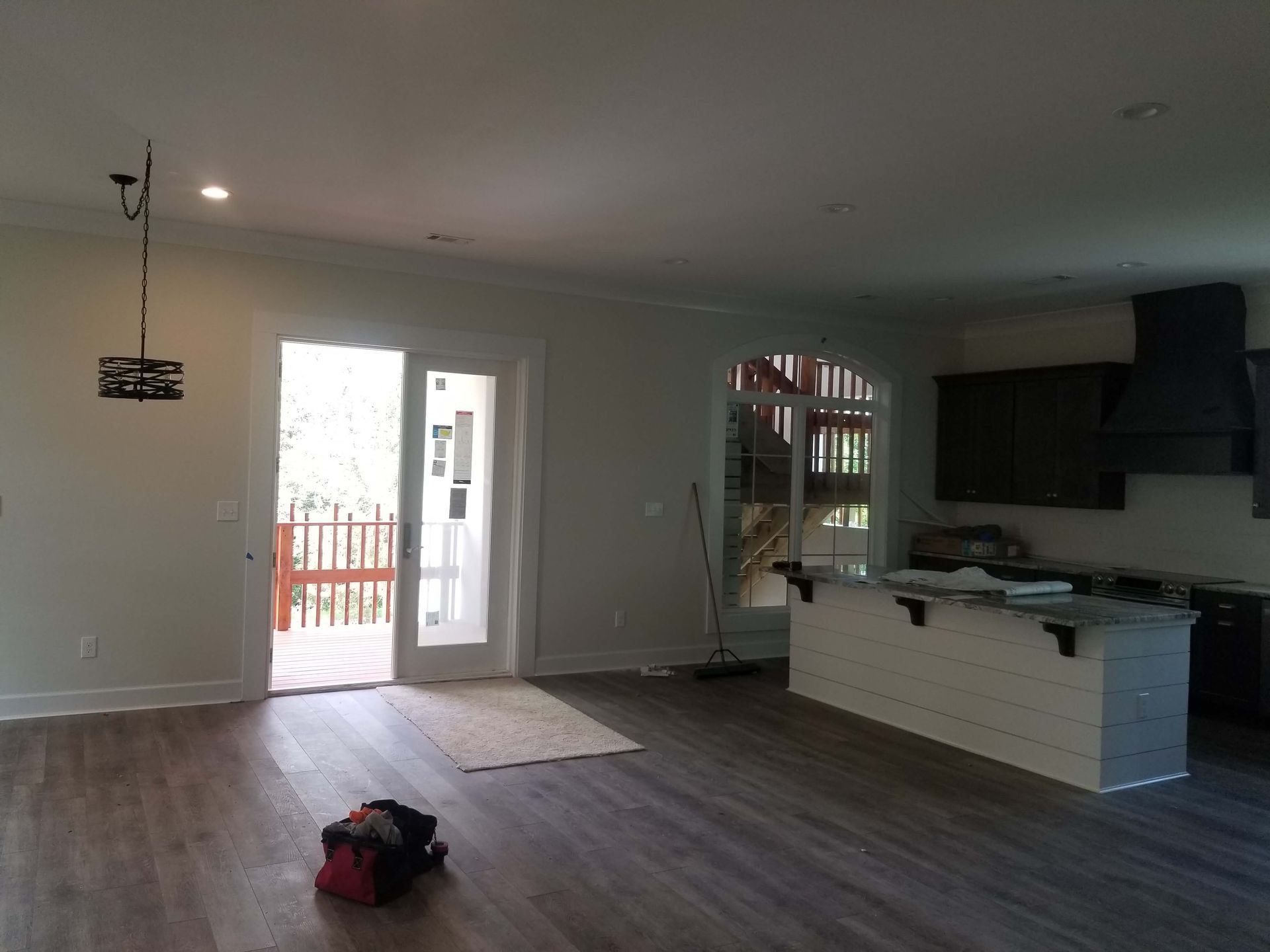 Open-concept kitchen and living area with light-colored walls, dark wood floors, and a door leading to a deck.