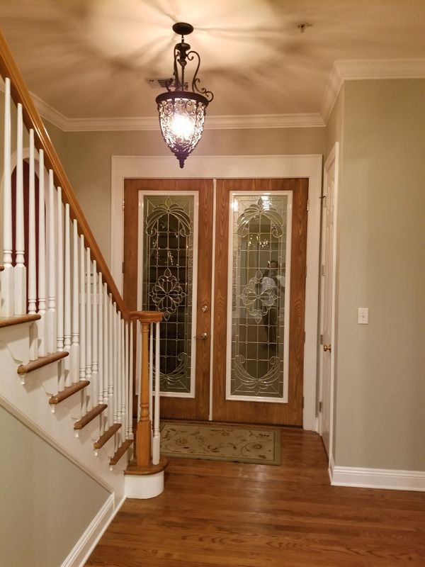 Entryway with wooden doors, staircase, and ornate chandelier. Light wood floors, light green walls.