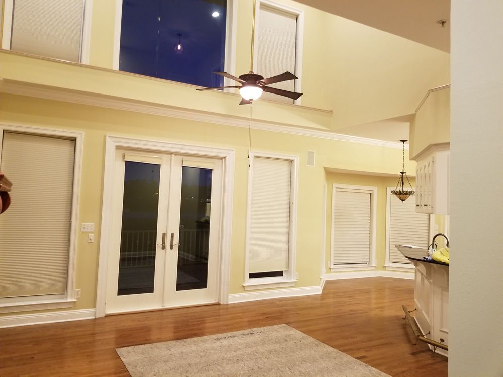 Spacious living room with French doors, windows with blinds, hardwood floors, and a ceiling fan.