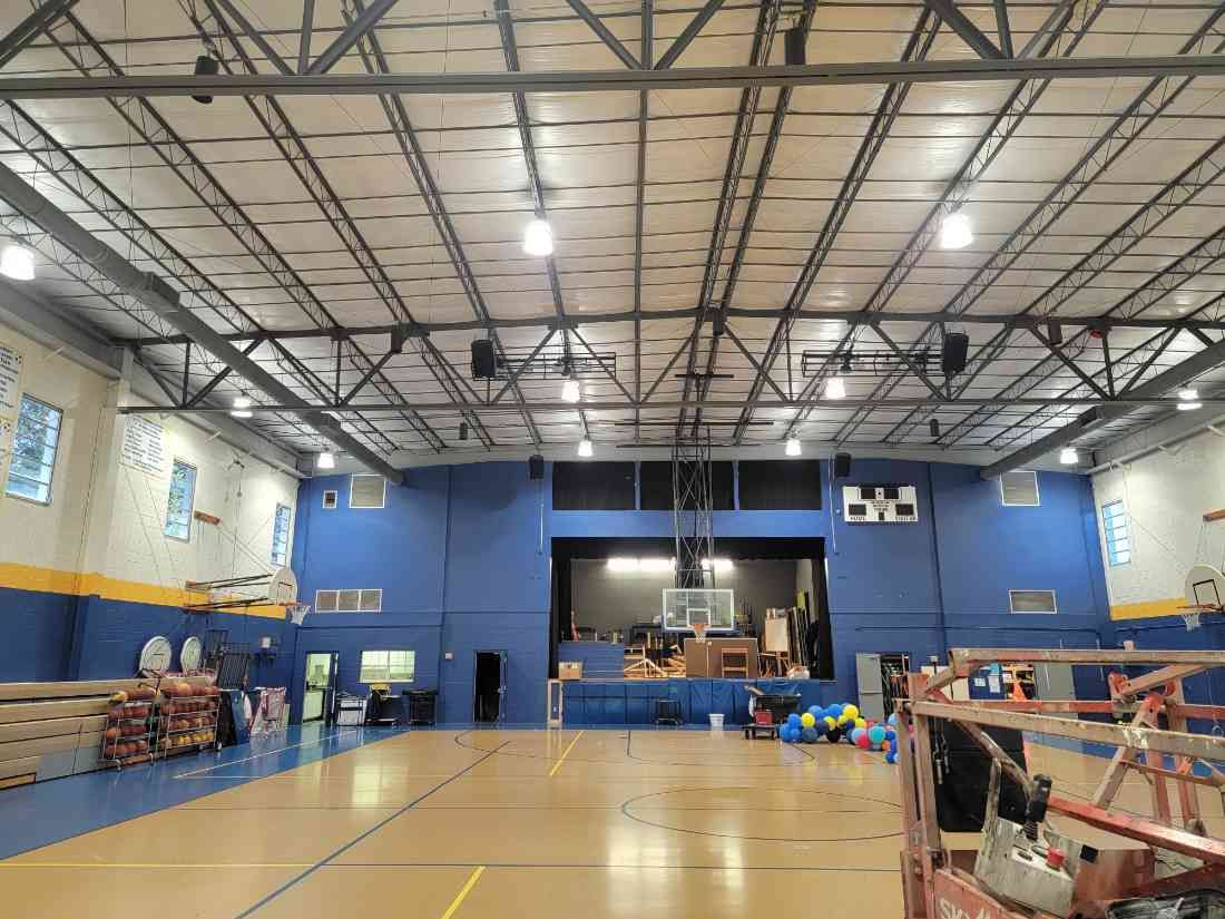 Gym interior with blue walls, a stage, basketball hoops, and a wooden floor.
