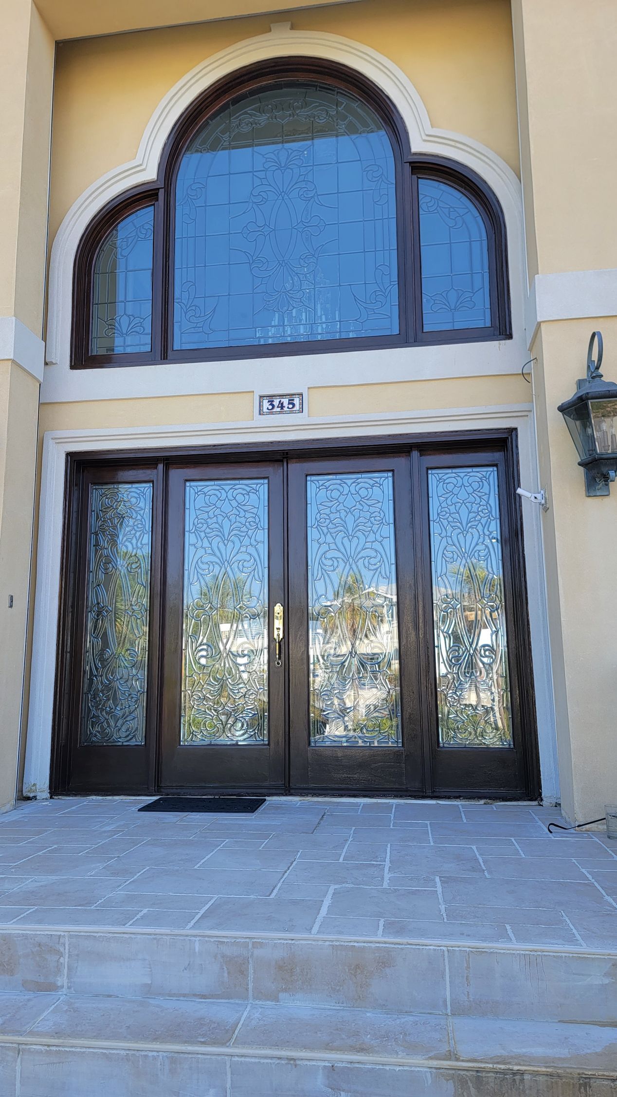 Double wooden doors with glass panels, topped by arched window. Stone steps lead to the entrance.
