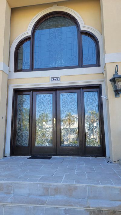 Brown double doors with glass panels and arched window above. Stone steps lead up to the entrance.