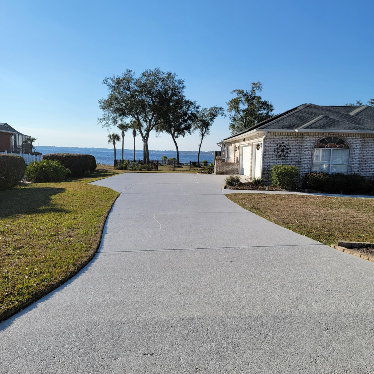Long driveway leading to a house, with trees and water in the background on a sunny day.