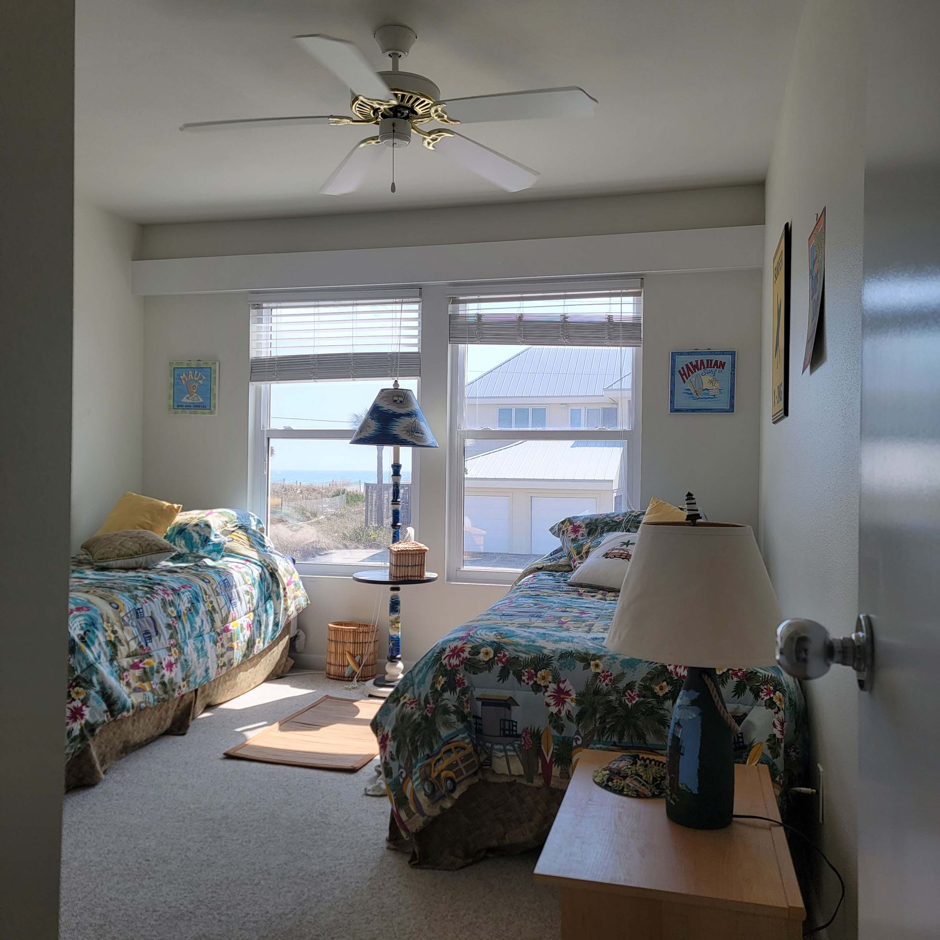 Bedroom with two twin beds, ocean view, blue floral bedding, lamp, and ceiling fan.