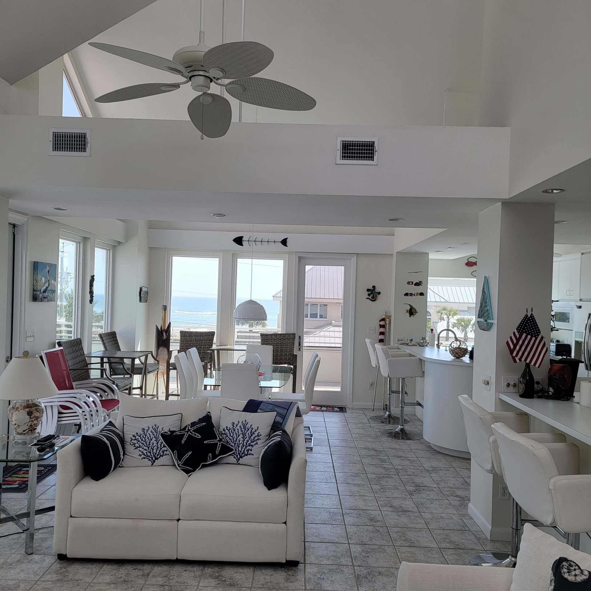 Bright, airy beach house interior with ocean view. White furniture, open floor plan, ceiling fan.