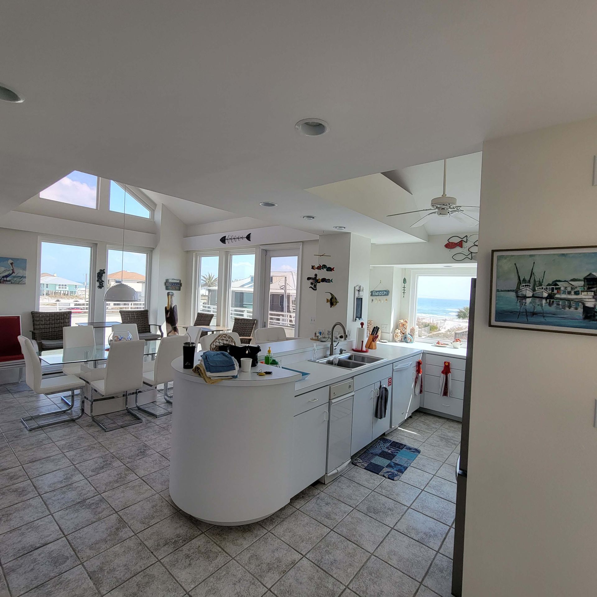 Bright white kitchen with curved island, dining area, and ocean view through windows.