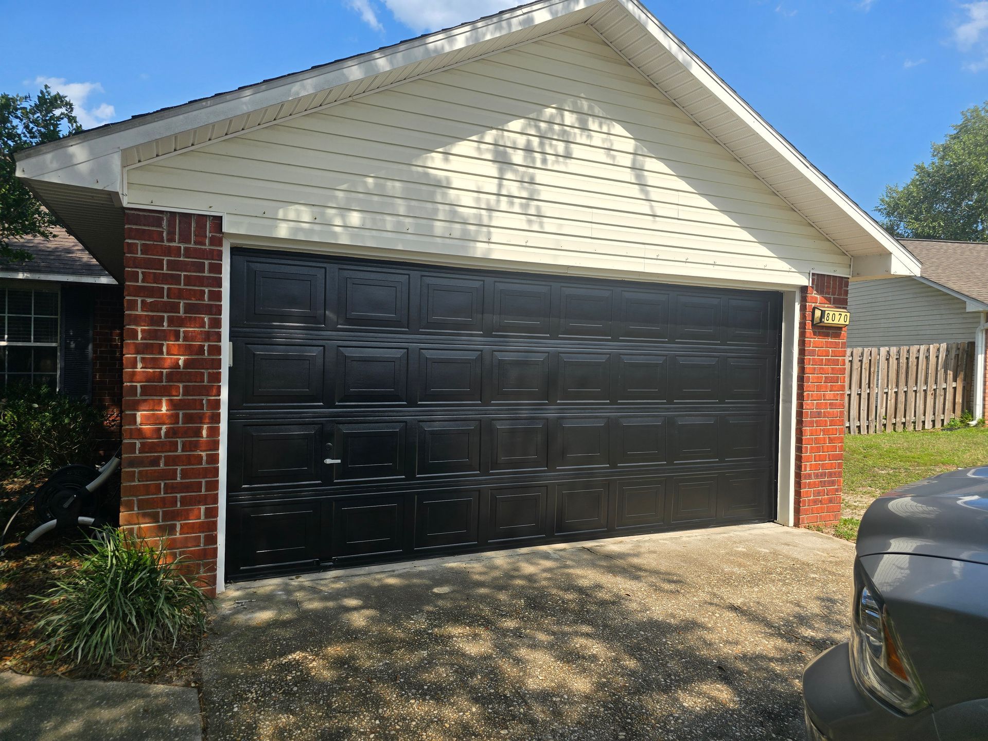 A black garage door on a residential home with red brick corners and a cream-colored shingled gable, viewed from outside.