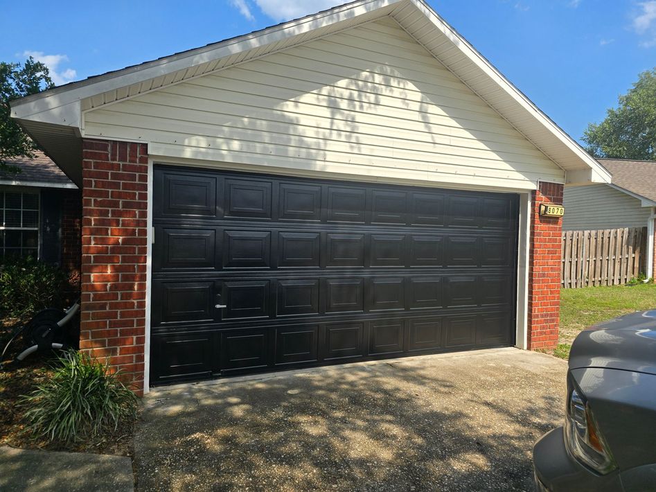 Black garage door with brick columns, beige siding, and blue sky.