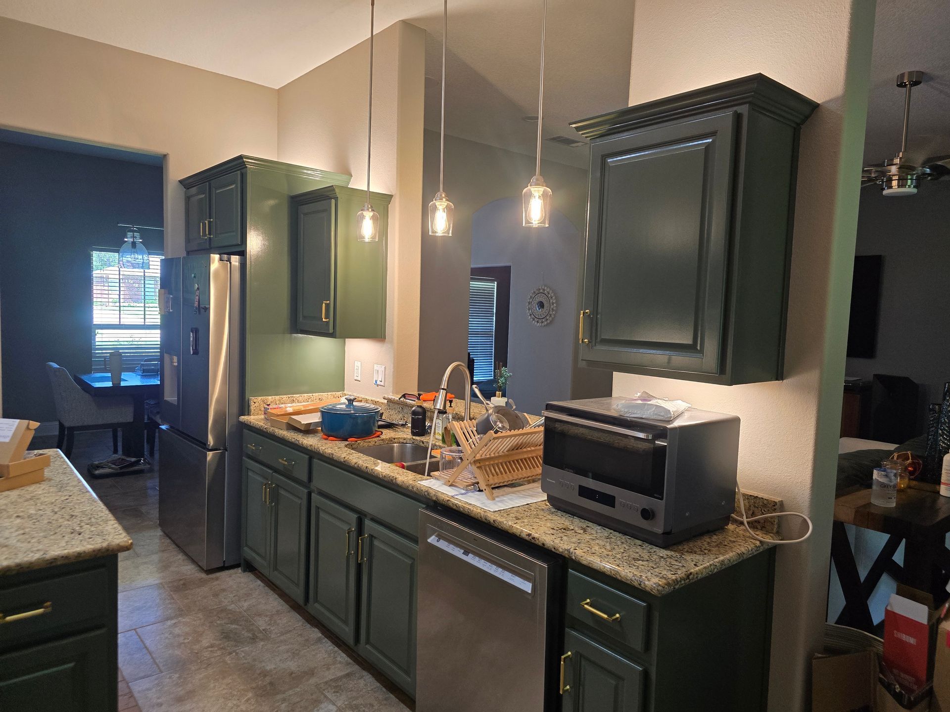 Modern kitchen with dark green cabinets, granite island, stainless fridge, and a toaster oven on the counter