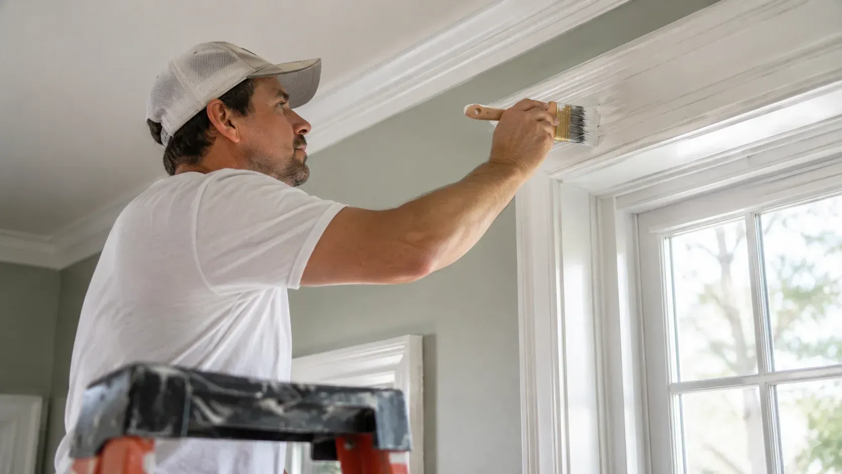 Painter applying white paint to interior window trim, showing how do you choose the right paint shee