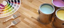 Paint cans and paintbrushes on a wooden floor next to a color palette.