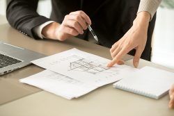 Two people reviewing building plans together at a desk. One points, the other holds a pen.