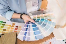 Person holding paint color swatches in various shades of blue and purple, inside.