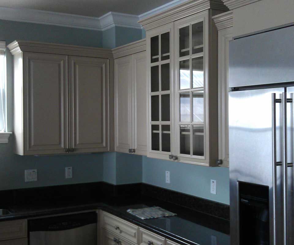 Kitchen cabinets with light-colored doors and a stainless steel refrigerator against a blue wall.
