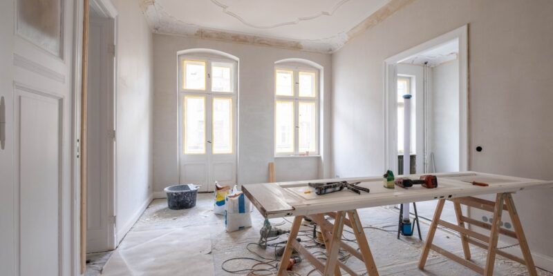 Room under renovation with tools on a workbench, two windows, and a partially finished ceiling.
