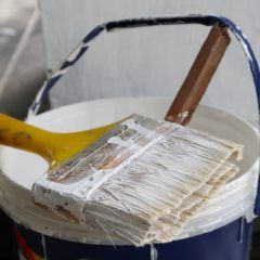 Paintbrush in white paint bucket with a wooden stick, close-up.