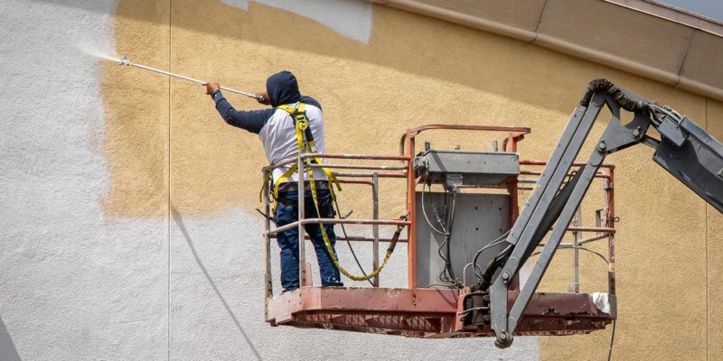 A worker paints a building exterior while standing in a lift.