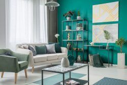 Living room with teal walls, sofa, shelving, art, and green and gray accents.
