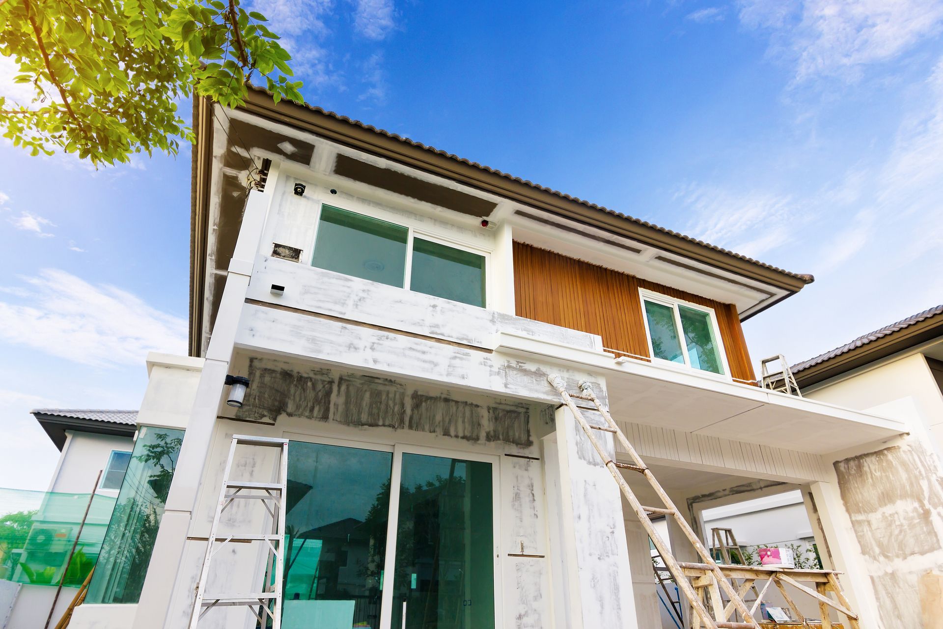 House exterior under construction with scaffolding, blue sky, and sunlight.
