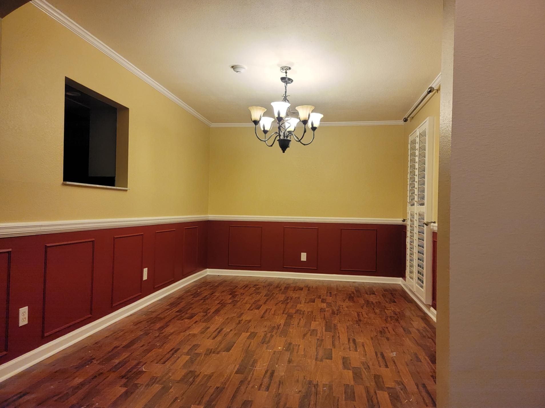Dining room with red wainscoting, yellow walls, wood floor, and a chandelier.