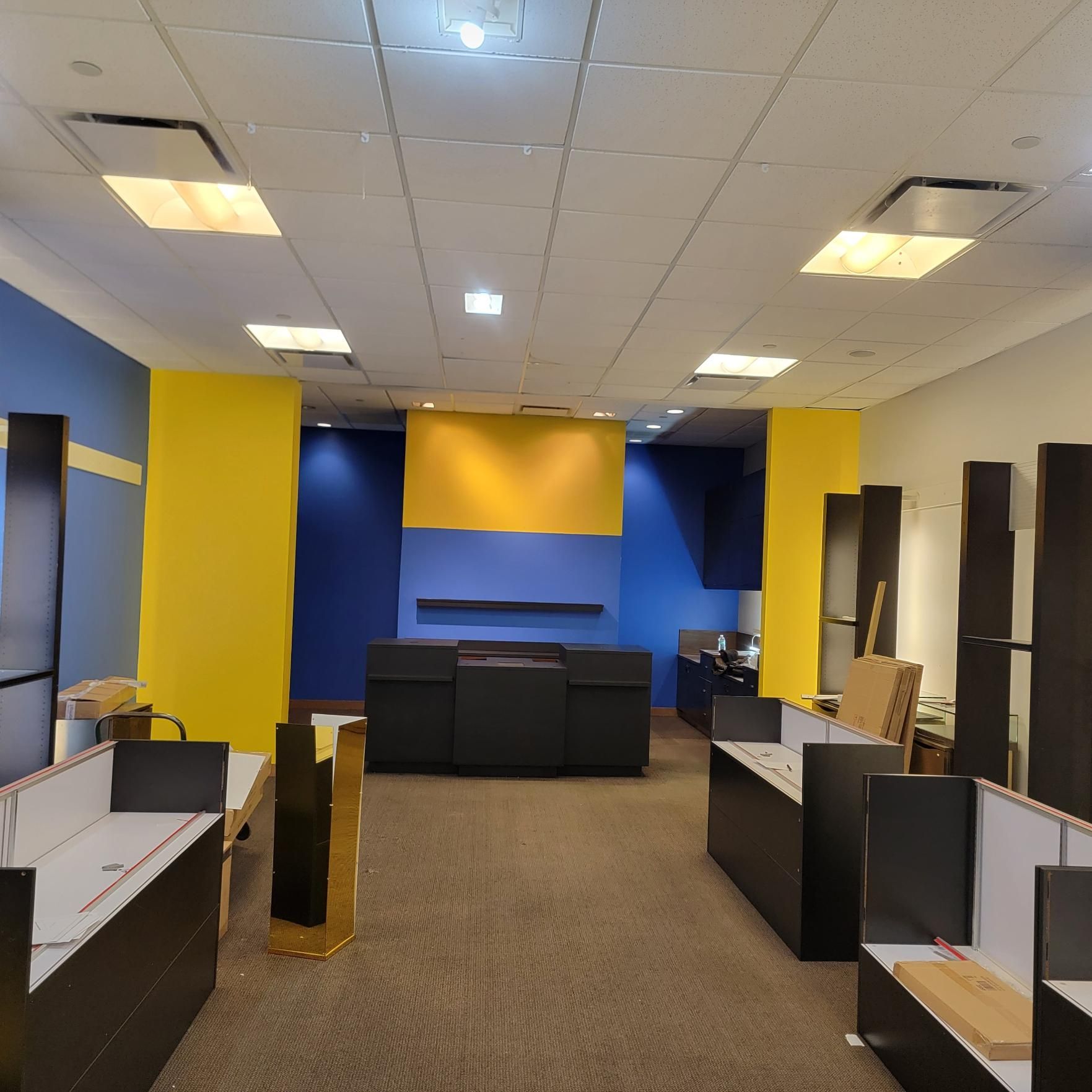 Empty office with blue, yellow, and black accents. Desks, cabinets, and carpeted floors.