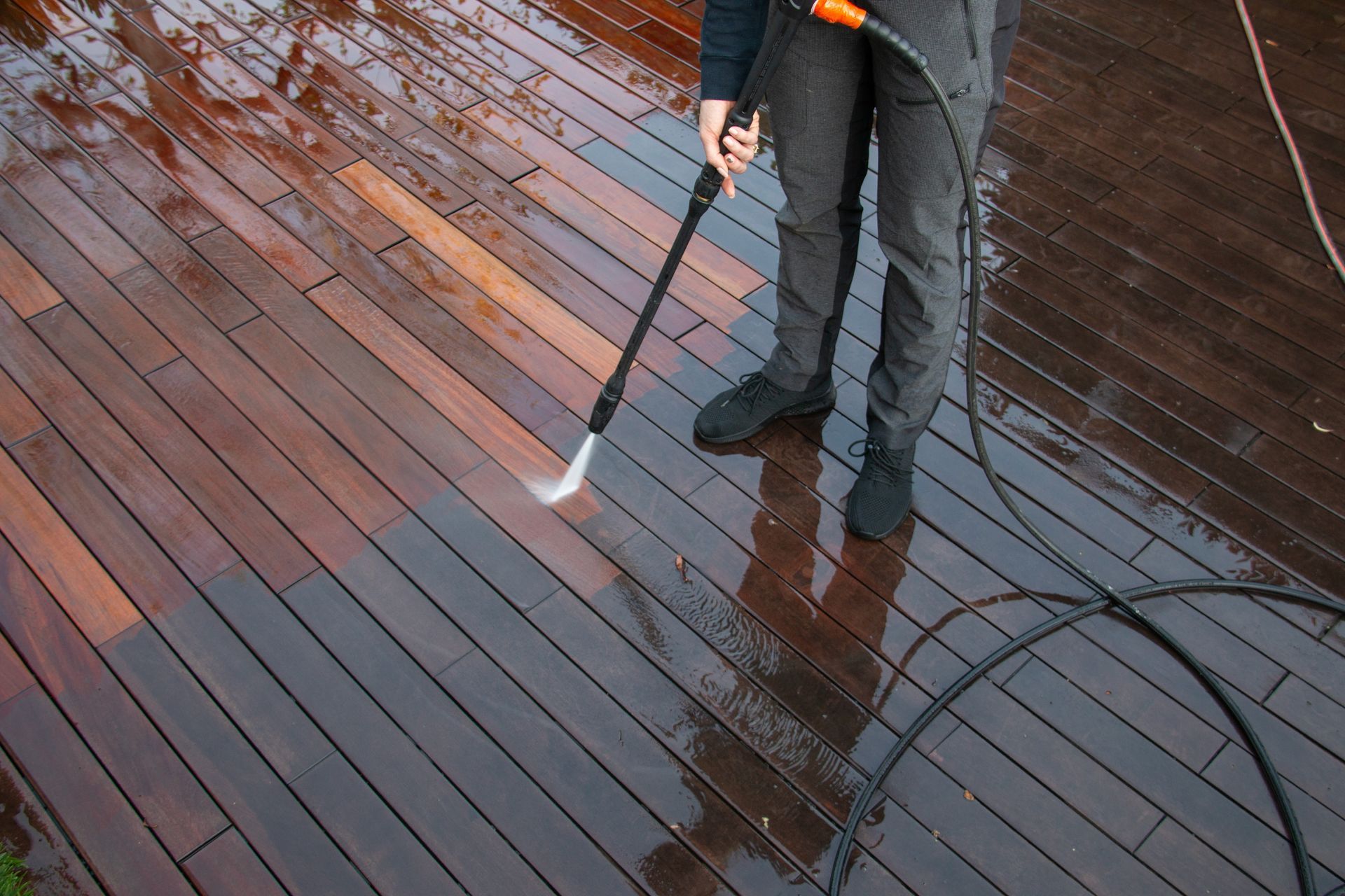 Person pressure washing a wooden deck, removing dirt and grime.