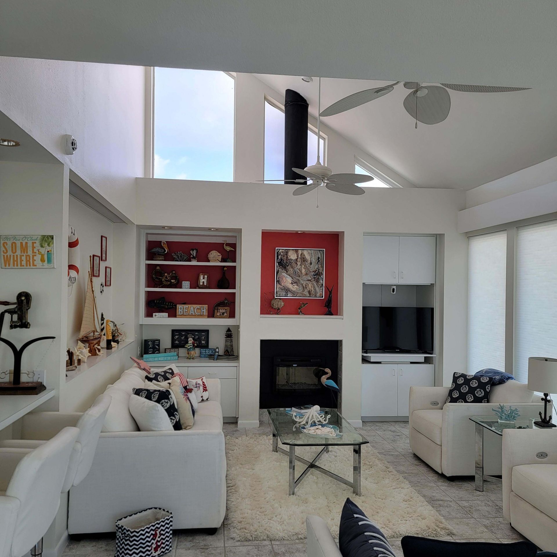 Bright living room with white couches, fireplace, and a high angled ceiling with windows.