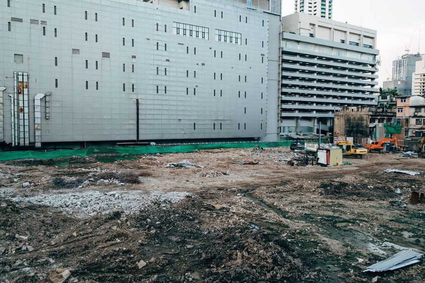 Empty urban lot beside tall gray buildings and a parked construction vehicle under an overcast sky