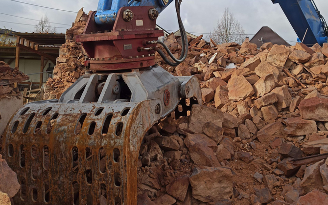 Excavator grapple lifting broken rocks at a construction or demolition site